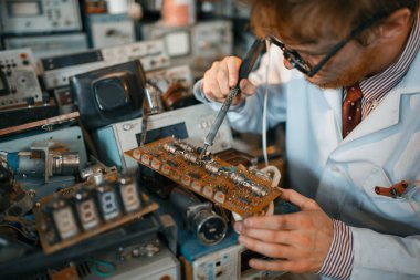 Garip bilim adamı lehimleme çipleri, laboratuvarda test. Arka planda elektriksel test araçları. Laboratuvar ekipmanları, mühendislik atölyesi