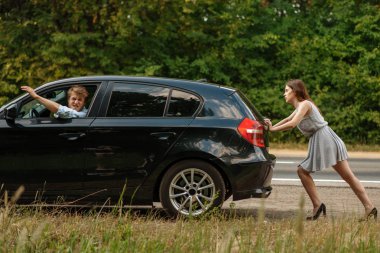 Genç bir kadın bozuk arabayı yolda bir adamla itiyor. Bozuk. Çarpışan otomobil ya da araçla acil durum kazası, otoyoldaki motor sorunu