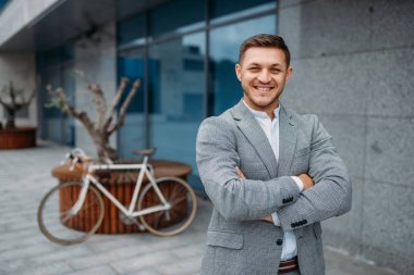 Şehir merkezindeki cam ofis binasında bisikletli gülümseyen bir işadamı. Şehir caddesinde çevre taşımacılığı yapan iş adamı, şehir tarzı.