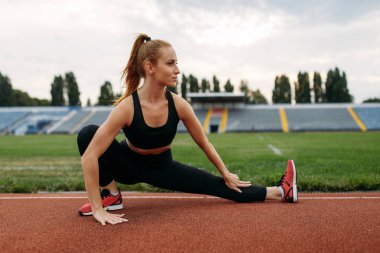 Spor giyim sektöründe bayan koşucu, stadyumda antrenman yapıyor. Kadın dışarıda koşmadan önce esneme egzersizi yapıyor.