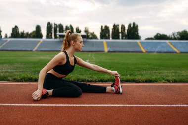 Spor giyim bölümünde bayan koşucu, stadyumda antrenman yapıyor. Kadın dışarıda koşmadan önce esneme egzersizi yapıyor.