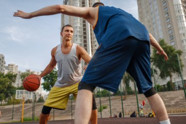 Basketbol sahasının ortasında açık sahada iki oyuncu. Spor giyim sektöründe erkek sporcular sokak topu antrenmanında oynuyor.