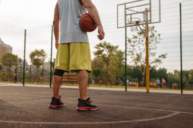 Basketbolcu erkek, basket topu dışarıda sahanın arka tarafında duruyor. Spor giyimli erkek sporcu sokak topu antrenmanında, yaz stadyumunda.