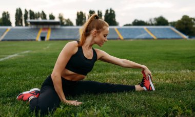Spor giyim bölümünde bayan koşucu, stadyumda antrenman yapıyor. Kadın dışarıda koşmadan önce esneme egzersizi yapıyor.