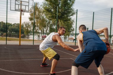 İki basketbolcu sahada yoğun bir maç yapıyor. Spor giyim sektöründe erkek sporcular sokak topu antrenmanında oynuyor.
