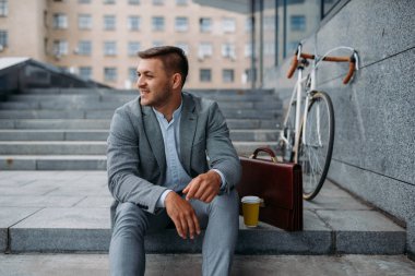 Bisikletli ve çantalı bir işadamı şehir merkezindeki ofis binasında öğle yemeği yiyor. Şehir caddesinde çevre taşımacılığı yapan iş adamı, şehir tarzı.