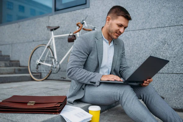 Businessman with bike and laptop having lunch at the office building in downtown. Business person riding on eco transport on city street, urban style