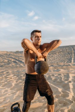 Erkek sporcu, güneşli bir günde çölde kettlebell ile egzersiz yapıyor. Sporda güçlü motivasyon, açık hava eğitiminde güçlü. 