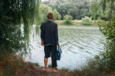 Takım elbiseli bir iş adamı, çantasıyla ıssız bir adada, arka planda duruyor. İş riski, çöküş veya iflas kavramı