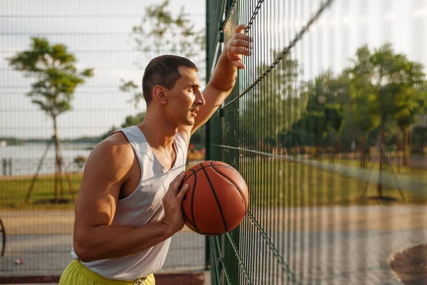 Férfi Kosárlabda Játékos Labdával Áll Rácsos Kerítésnél Szabadtéri Pályán Oldalnézetből — Stock Fotó