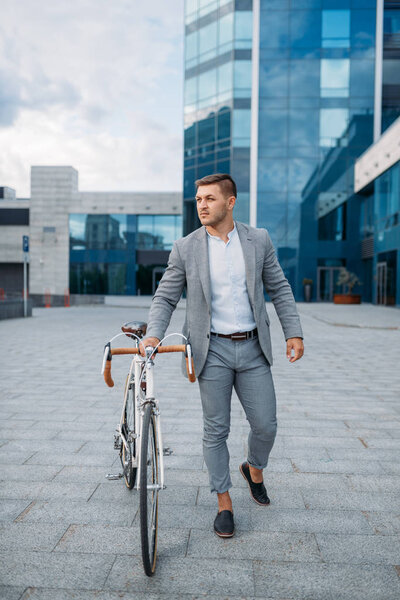 Businessman in suit with bicycle in downtown. Business person riding on eco transport on city street