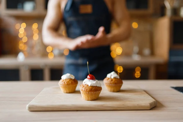 Naked man in apron cooking cakes with cherry on the kitchen. Nude male person preparing breakfast at home, food preparation without clothes