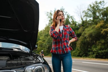 Genç bir kadın yolda bir çekiciyi arıyor, araba arızalı. Bozuk otomobil veya araçla acil durum kazası, otoyoldaki motor arızası
