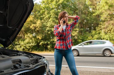 Genç bir kadın yolda bir çekiciyi arıyor, araba arızalı. Bozuk otomobil veya araçla acil durum kazası, otoyoldaki motor arızası