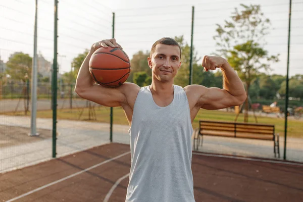 男子篮球运动员带着球在室外场地上展示他的肌肉 男子运动员穿着运动服参加街球训练 夏季体育场 — 图库照片