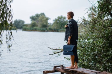 Takım elbiseli bir iş adamı, çantasıyla ıssız bir adada, arka planda duruyor. İş riski, çöküş veya iflas kavramı