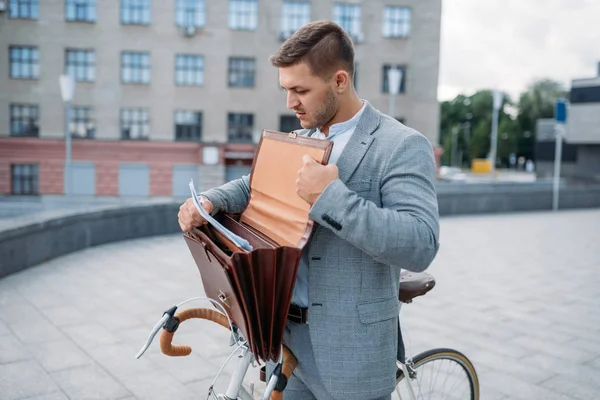 One businessman biking in suit with briefcase in downtown. Business person riding on eco transport on city street