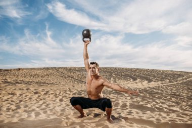 Erkek sporcu, güneşli bir günde çölde ağırlıklarla egzersiz yapıyor. Sporda güçlü motivasyon, açık hava eğitiminde güçlü.