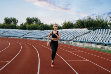 Spor giyimde koşan bayan koşucu, stadyumda antrenman yapıyor. Kadın dışarıda koşmadan önce esneme egzersizi yapıyor.