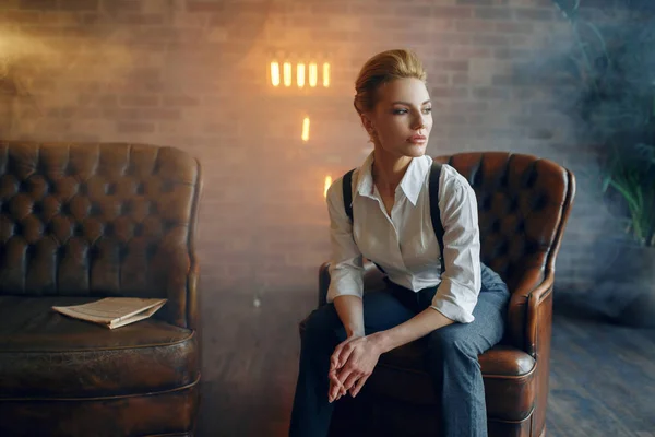 エレガンスビジネス女性で厳格な服姿勢で革ソファでスタジオ レトロファッション ギャングスタイル マフィア — ストック写真