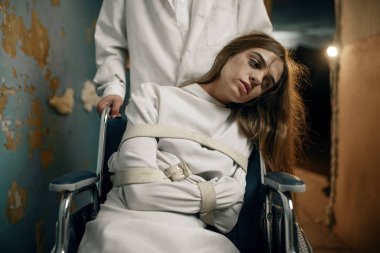 Erkek psikiyatrist ve deli kadın hasta tekerlekli sandalyede, akıl hastanesinde. Deli gömleği giyen kadın akıl hastası olduğu için klinikte tedavi görüyor.