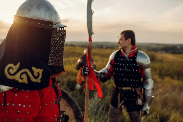 Medieval knights in armor and helmet at sunset, great tournament. Armored ancient warrior in armour posing in the field
