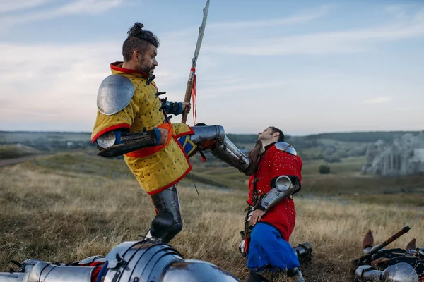 Old medieval knight in armor prepares to cut off head, great battle. Armored ancient warrior in armour posing in the field