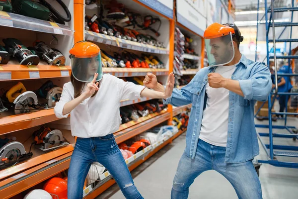 Playful couple fight in hardware store like a children. Male and female customers look at the goods in diy shop