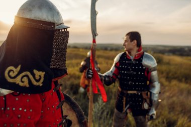 Gün batımında zırhlı ve miğferli ortaçağ şövalyeleri, büyük turnuva. Zırhlı eski bir savaşçı tarlada poz veriyor.
