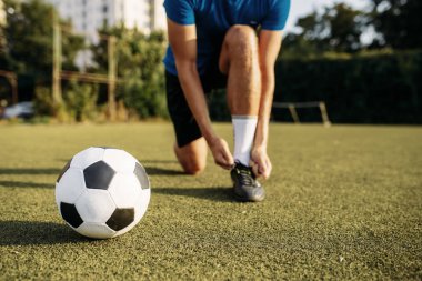 Erkek futbolcu ayakkabı bağcıklarını botlara bağlıyor. Açık stadyumdaki futbolcu, maçtan önce antrenman, futbol antrenmanı.