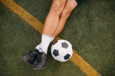 Sahada çimlerin üzerinde oturan erkek futbolcu. Açık stadyumdaki futbolcu, maçtan önce antrenman, futbol antrenmanı.