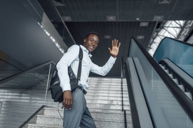 Mutlu Afrikalı işadamı alışveriş merkezinde yürüyen merdivenden çıkıyor. Başarılı iş adamı, resmi giyinmiş siyah adam, alışveriş merkezi. 