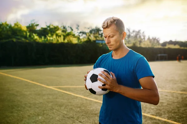 Male soccer player with ball in hands on the field. Footballer on outdoor stadium, workout before game, football training