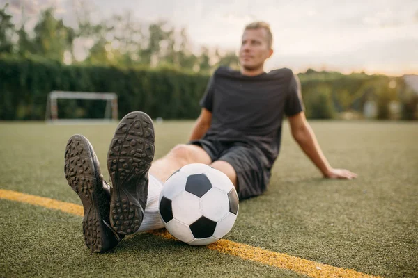 フィールド上の芝生の上に座ってボールを持つ男性サッカー選手 屋外スタジアムでのサッカー ゲームの前にトレーニング サッカーのトレーニング — ストック写真