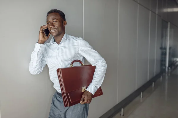 在办公室走廊里拿着公事包的非洲商人通过电话交谈 — 图库照片