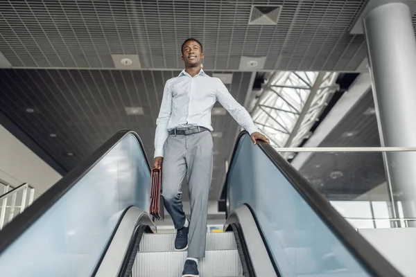 african businessman with briefcase descending on the escalator in mall