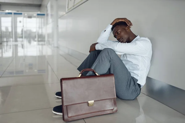 一个拿着公文包坐在办公室走廊地板上的非洲商人 累了的商人 — 图库照片