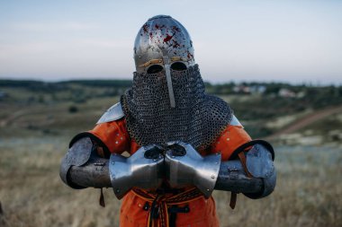 Metal zırhlı ortaçağ şövalyesi kılıç tutuyor, büyük savaş. Zırhlı eski bir savaşçı tarlada poz veriyor.