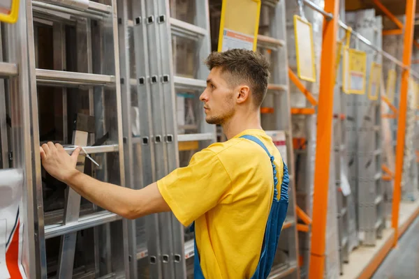 Male constructor choosing the stairs in hardware store. Builder in uniform look at the goods in diy shop