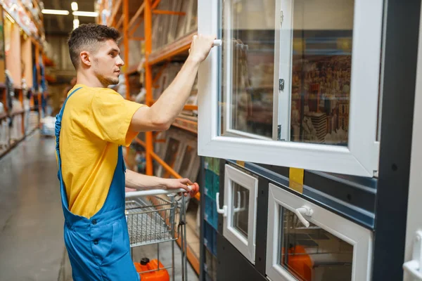 Male constructor choosing windows in hardware store. Builder in uniform look at the goods in diy shop
