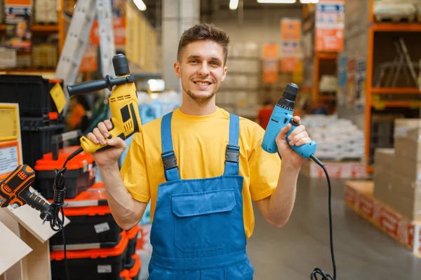 Male builder with power tools in hardware store. Constructor in uniform look at the goods in diy shop