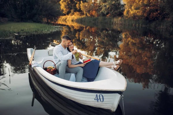 Love couple with fruit basket lying in a boat on quiet lake at summer day. Romantic meeting, boating trip, man and woman walking along the river