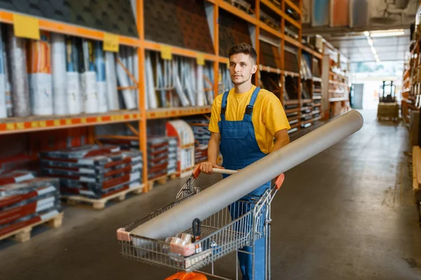 Male builder carries building materials in a cart, hardware store. Customer look at the goods in diy shop