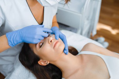 Eldivenli kozmetik uzmanı tedavi masasındaki kadın hastaya yüz botoksu yapar. Güzellik salonunda gençleştirme prosedürü. Doktor ve kadın, kırışıklıklara karşı estetik ameliyat.