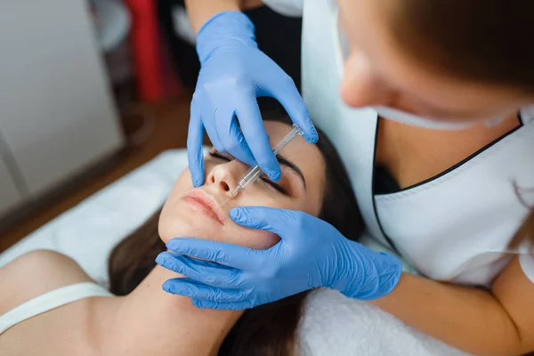 Cosmetician in gloves gives face botox injections to female patient on treatment table. Rejuvenation procedure in beautician salon. Doctor and woman, cosmetic surgery against wrinkles