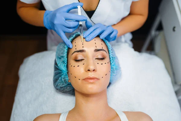 Cosmetician makes botox injection in dotted lines on female patient face, botox injections preparation. Rejuvenation procedure in beautician salon. Cosmetic surgery against wrinkles and aging