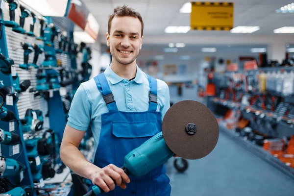 stock image Male worker in uniform holds angle grinder in tool store. Choice of professional equipment in hardware shop, instrument supermarket