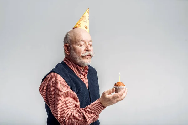 Улыбающийся Пожилой Мужчина Шапочке Вечеринок Показывает Торт Свечой Серым Фоном — стоковое фото