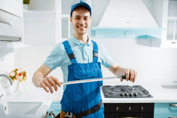 Üniformalı Gülümseyen Erkek Mobilyacı Mutfakta Şerit Tutuyor Tamirci Garnitür Kuruyor — Stok fotoğraf