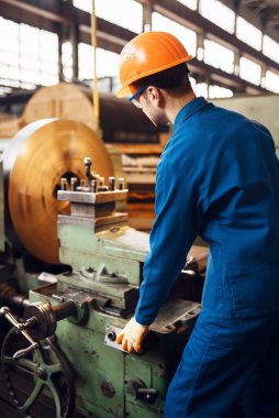 Üniformalı ve kasklı Turner torna tezgahında çalışıyor. Endüstriyel üretim, metal mühendisliği, güç makineleri üretimi